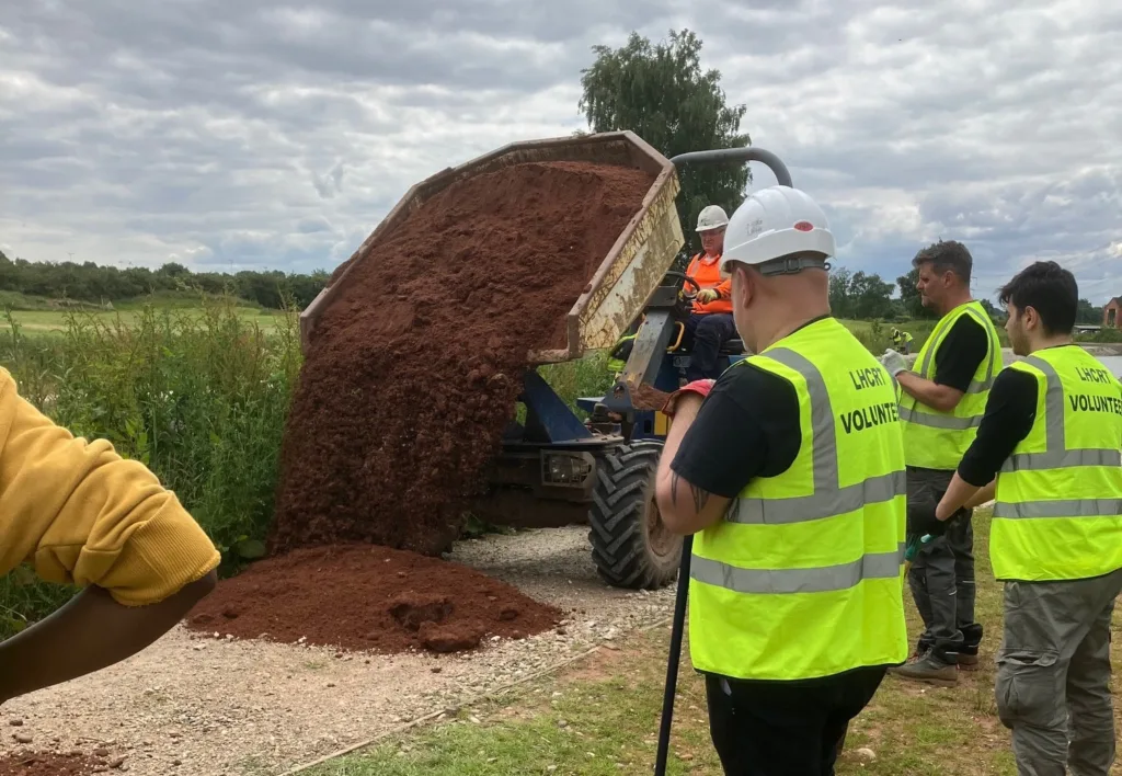 A group of volunteers watching sand being unloaded from a dumper truck